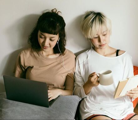 Two women working in bed reading and drinking coffee